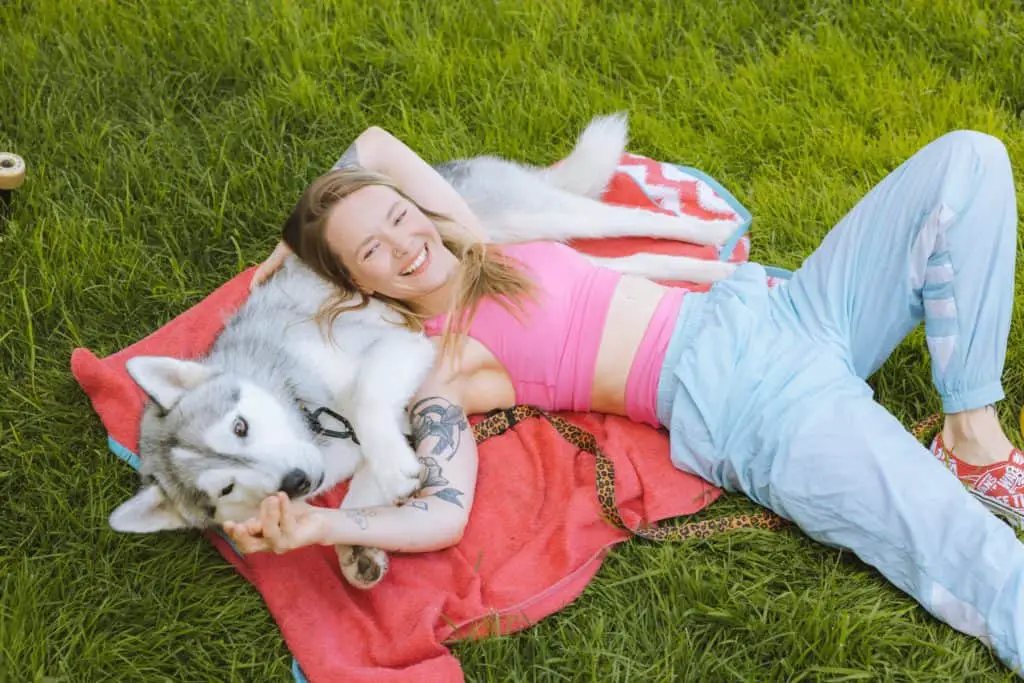 Woman lying on Husky's stomach while on a blanket in the grass